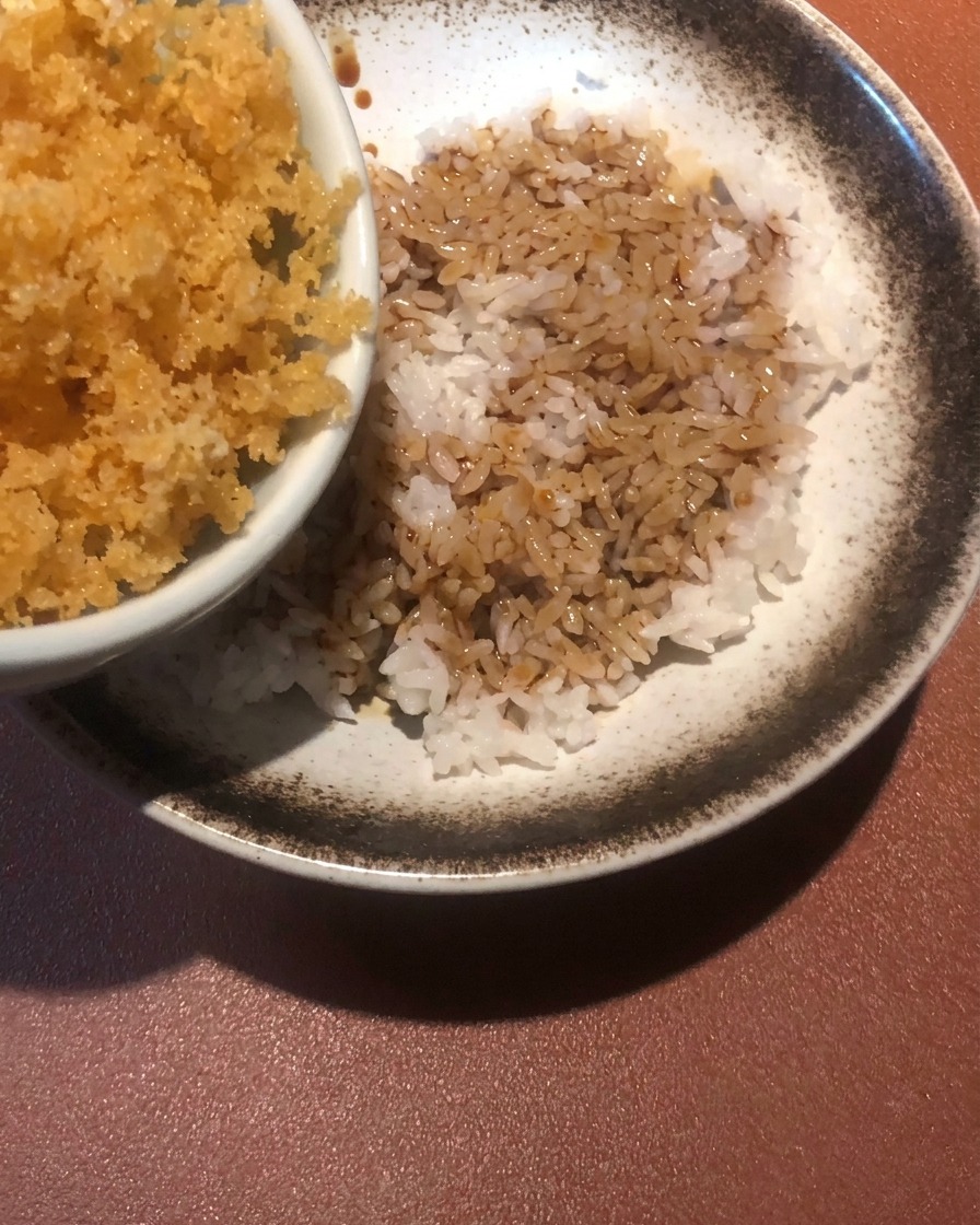 Crispy, golden-brown fried batter crumbs being scattered over a bowl of rice and sauce.