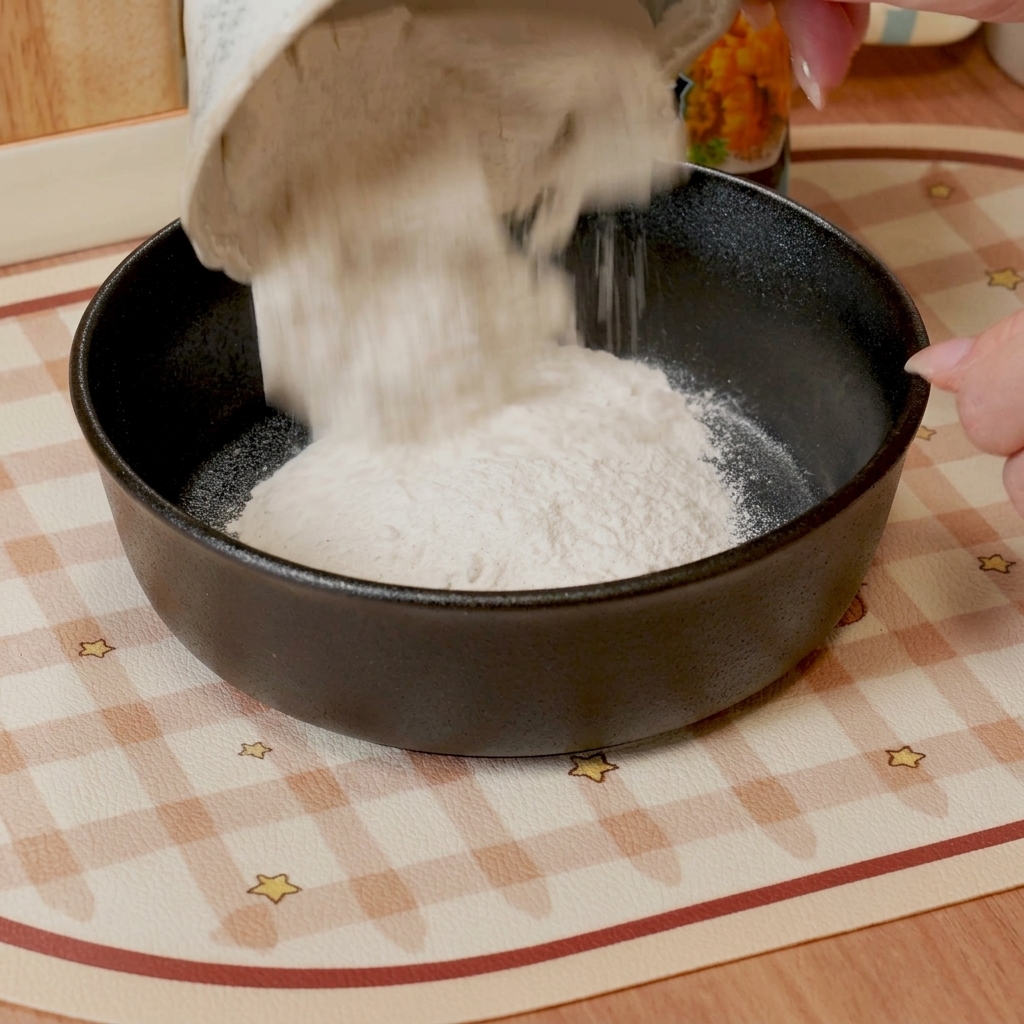 A whisk mixing tempura flour and water into a smooth, thin batter in a dark-colored bowl.