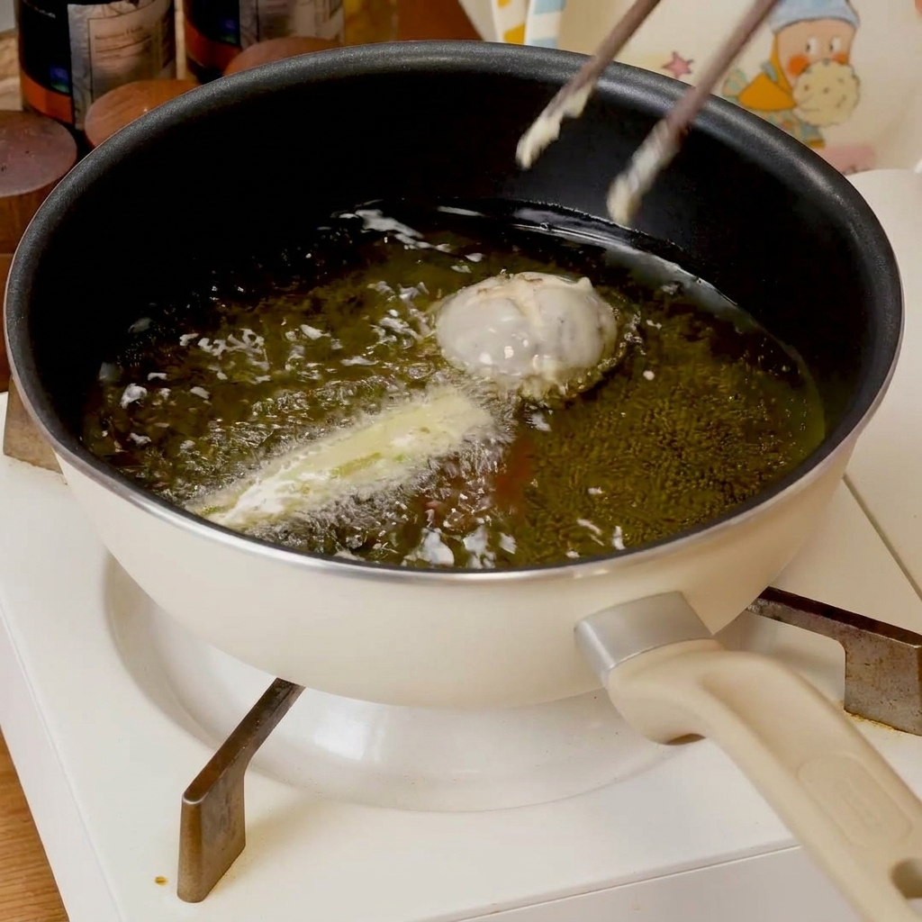 Battered tempura pieces sizzling in a shallow pan of hot oil, turning golden brown.