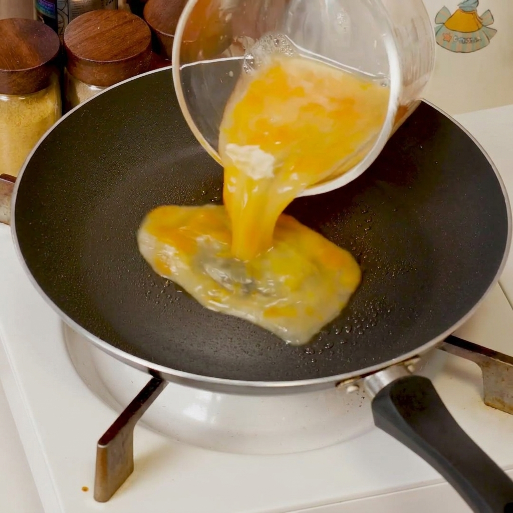 Beaten eggs cooking in a pan, being pushed toward the center with a spatula to form soft curds.