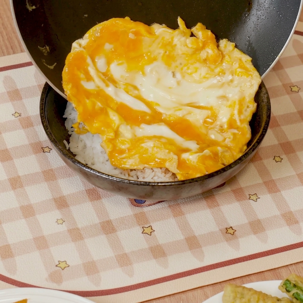 Soft-scrambled eggs with sauce being slid onto a bowl of white rice.