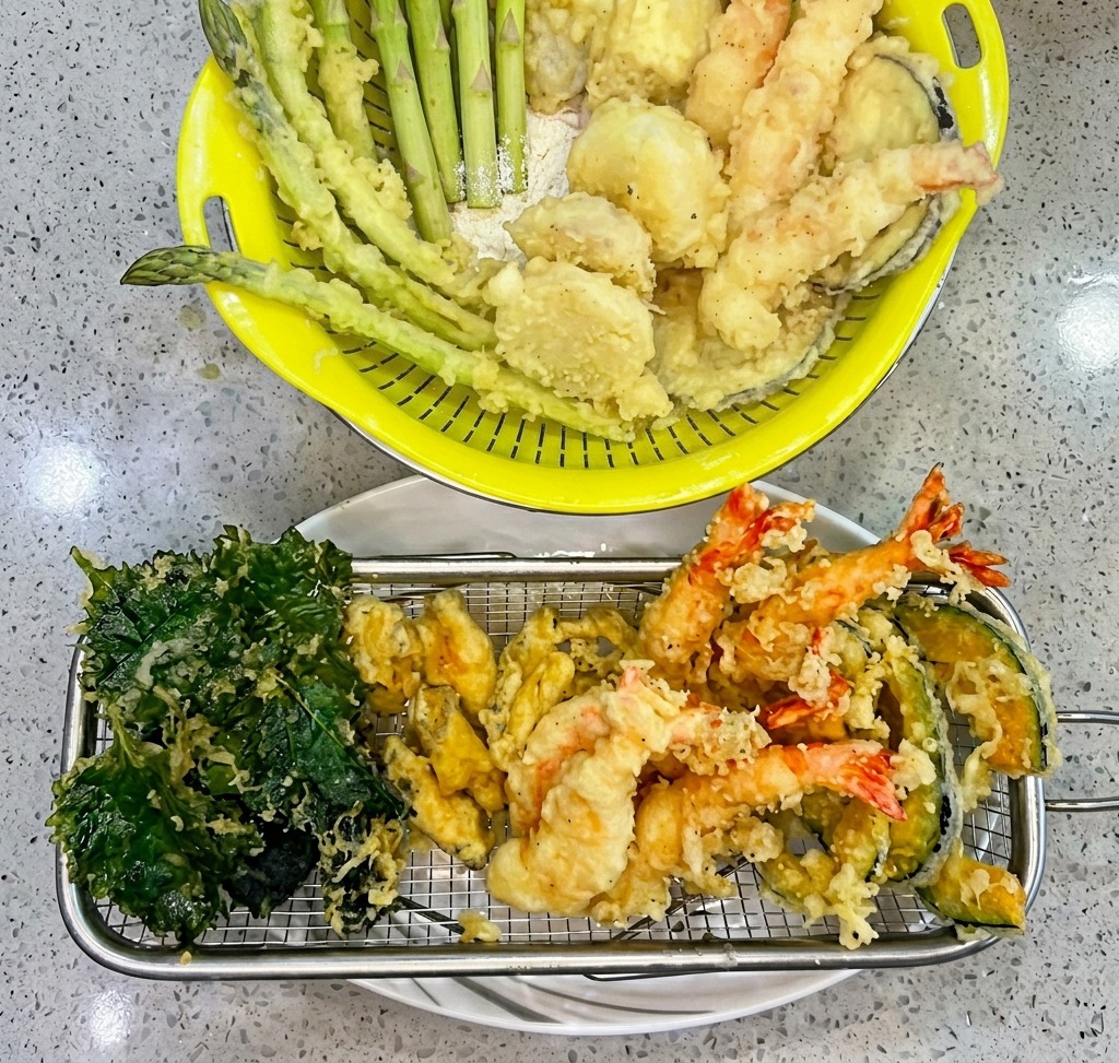 Shrimp coated in tempura batter being lowered into hot oil in a deep frying basket.
