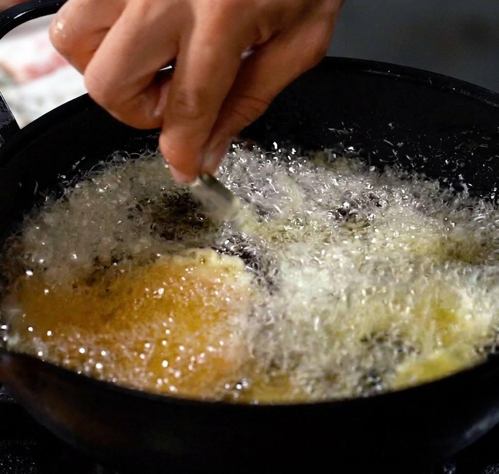 Shrimp frying in a deep pot of hot oil, creating a golden, crispy coating.