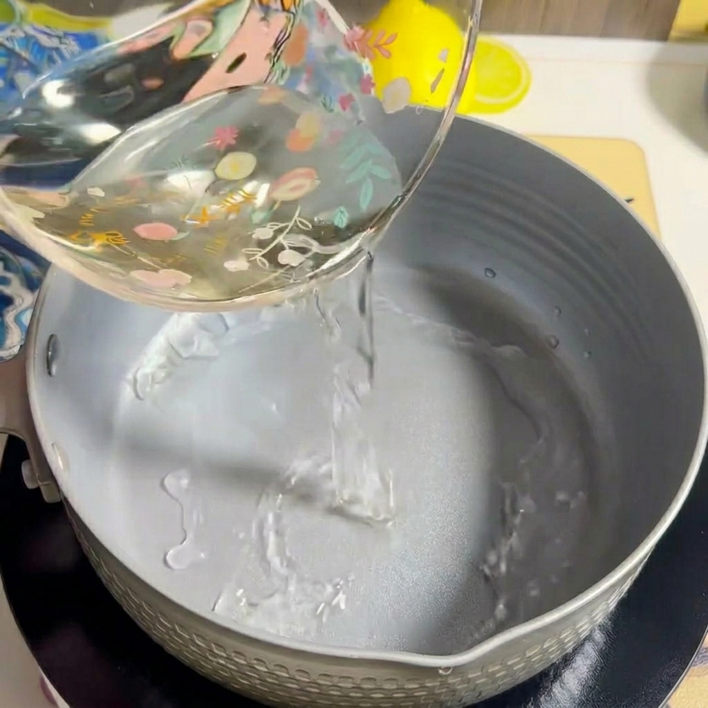 Water being poured into an empty grey cooking pot on a stovetop.