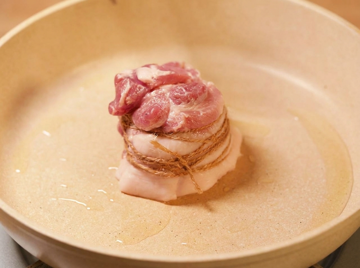 The tied pork belly searing in a pan with hot oil until the surface is golden brown.