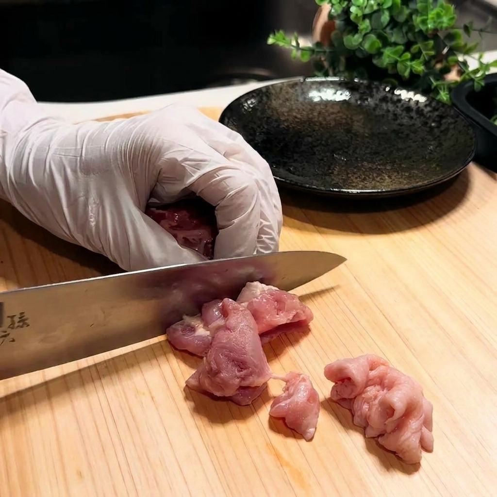 Close-up of chicken thigh being sliced into small pieces on a wooden cutting board.