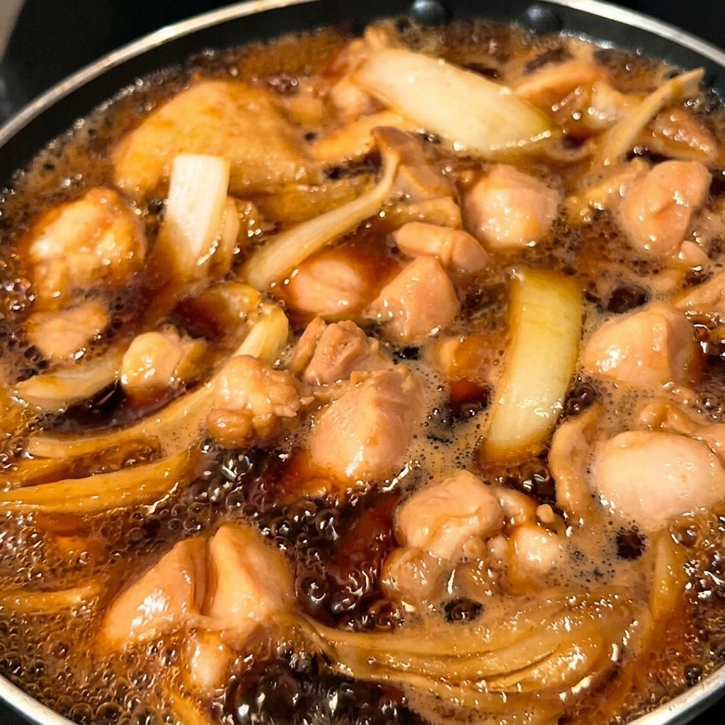 Half of the beaten egg mixture being poured into the pan over the chicken and onions.