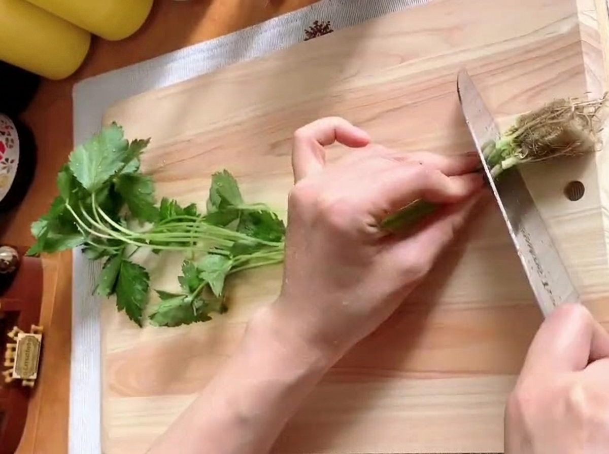 Fresh mitsuba stems being cut into segments on a wooden board.