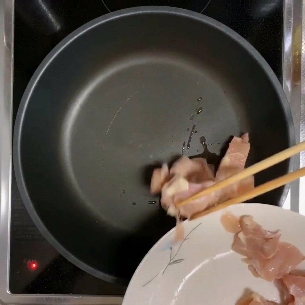 Chicken pieces being placed into a preheated, oiled pan.