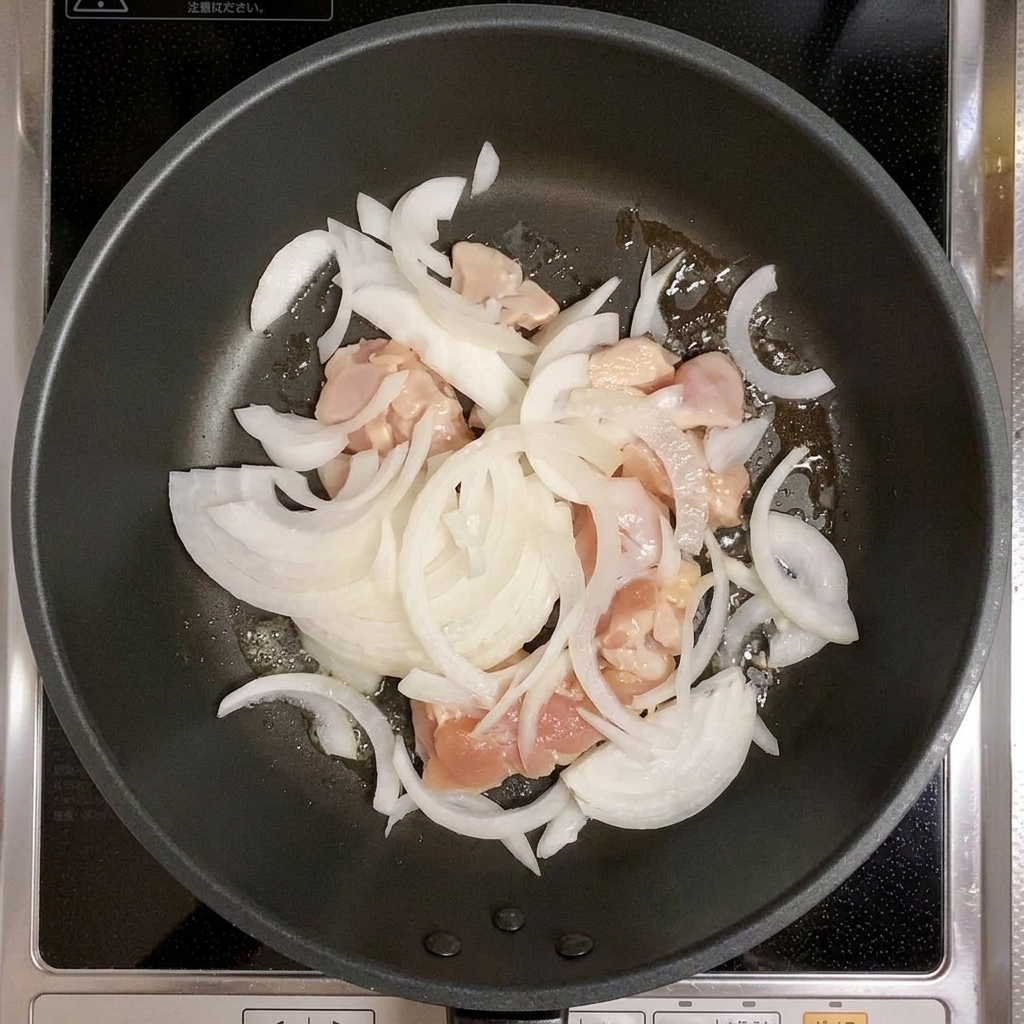 Chicken and sliced onions being stirred together in a frying pan.