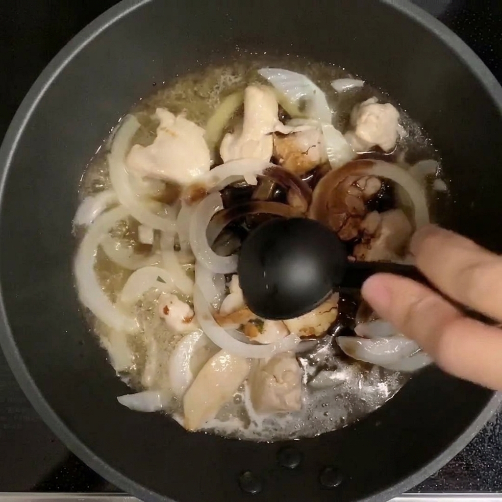 Measuring spoon pouring seasonings into a pan with chicken and onion simmering in dashi.