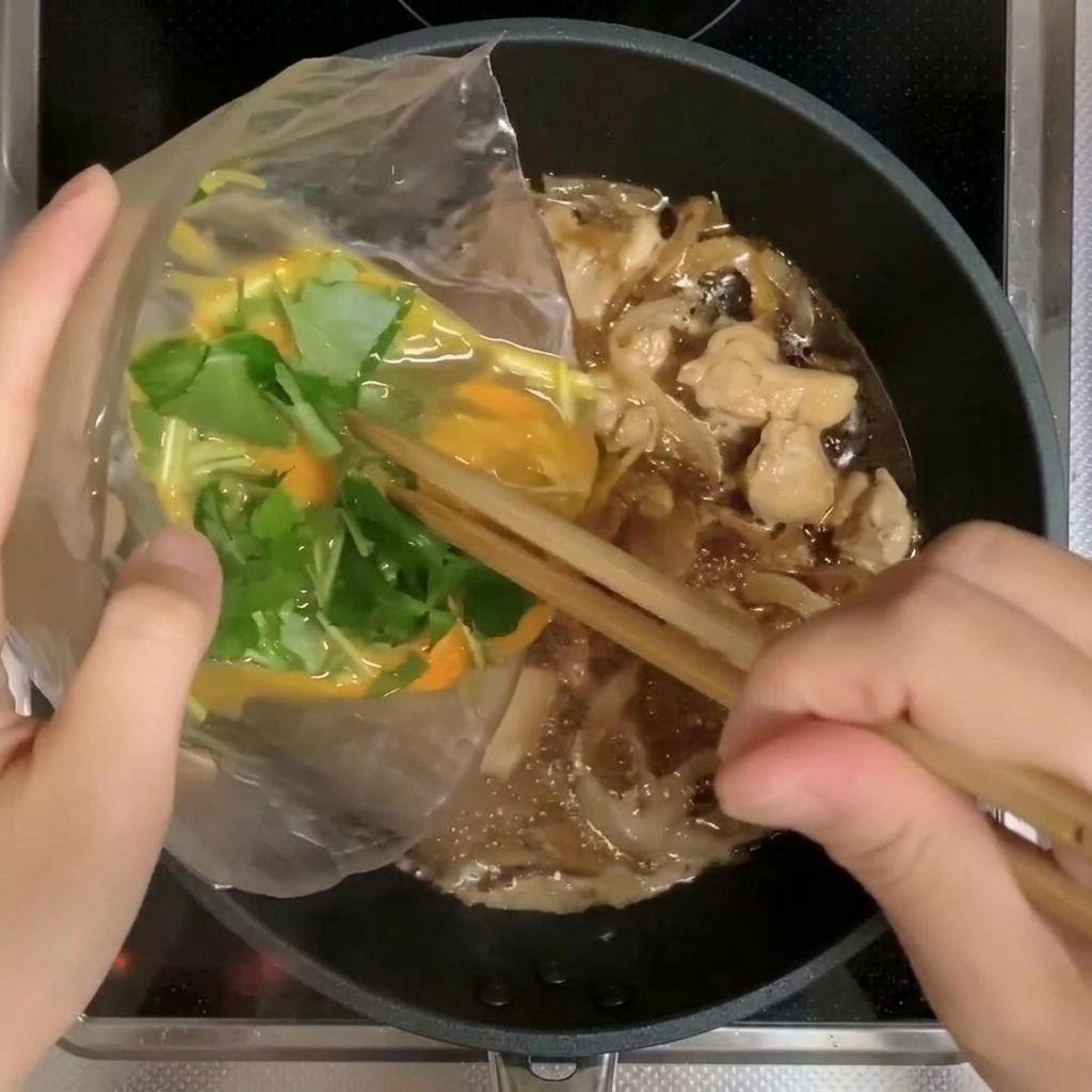 Two-thirds of the egg and mitsuba mixture being poured into the pan with chicken and onions.