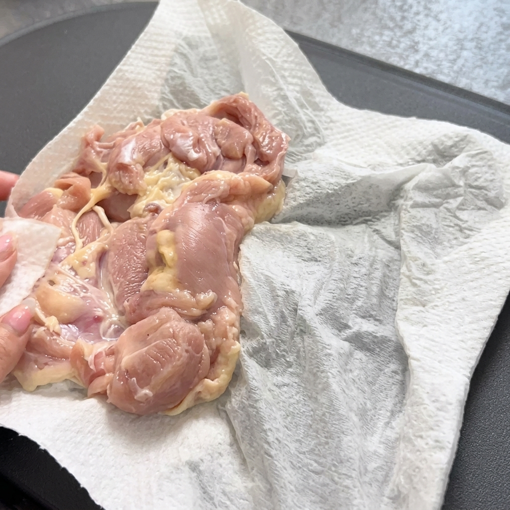 Using tongs to gently place a raw chicken thigh into a hot, preheated frying pan.