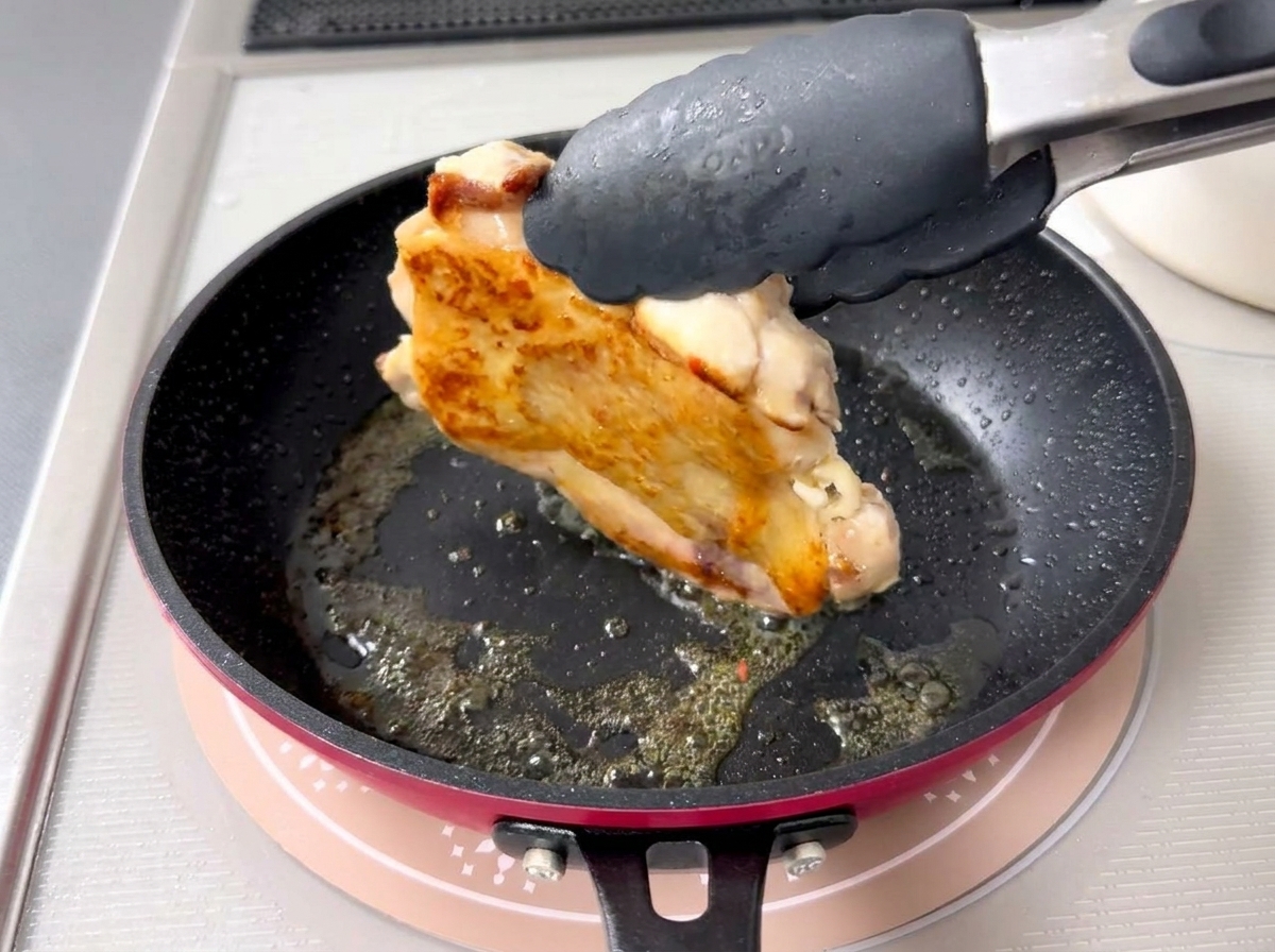 Close-up of a pair of tongs flipping a piece of chicken to reveal perfectly browned, crispy skin.
