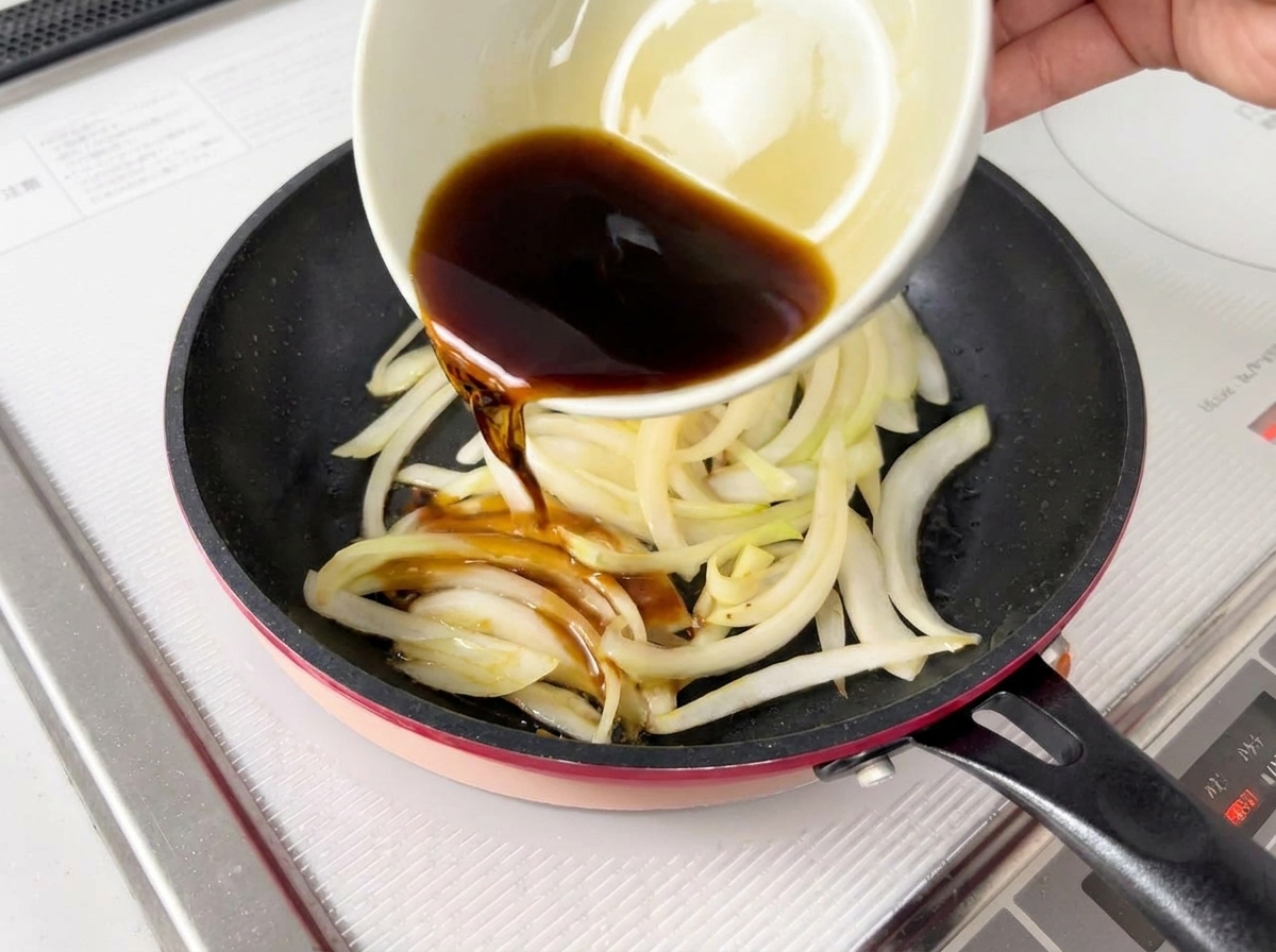 Dark sauce being poured from a white bowl over softened onions in a pan.