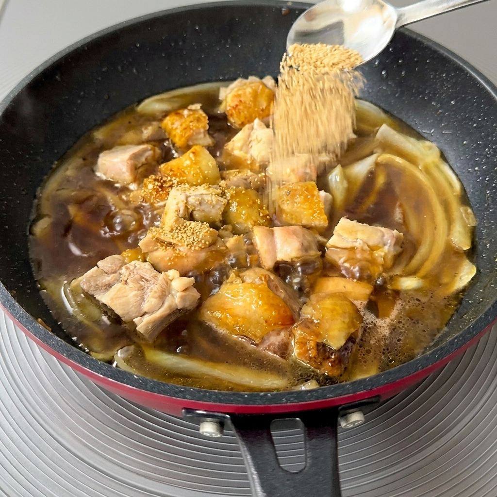 Close-up of a spoonful of golden dashi granules being sprinkled into a simmering pan of chicken and onions.