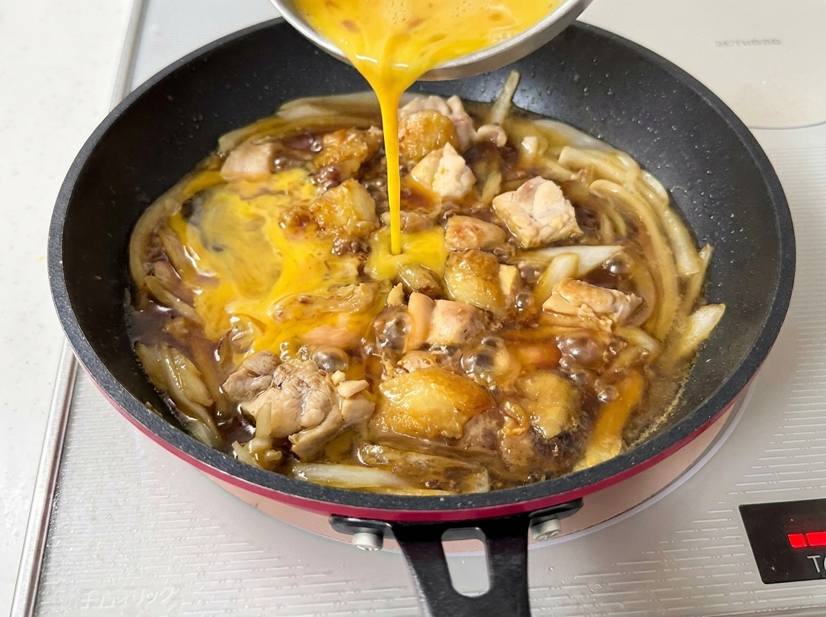 Beaten eggs being poured from a bowl into the pan, coating the simmering chicken and onions.