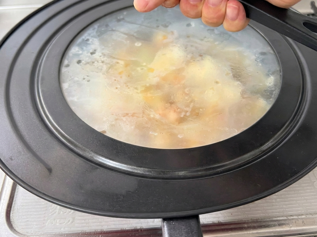 A glass lid being placed onto a red frying pan, with steam visible inside.