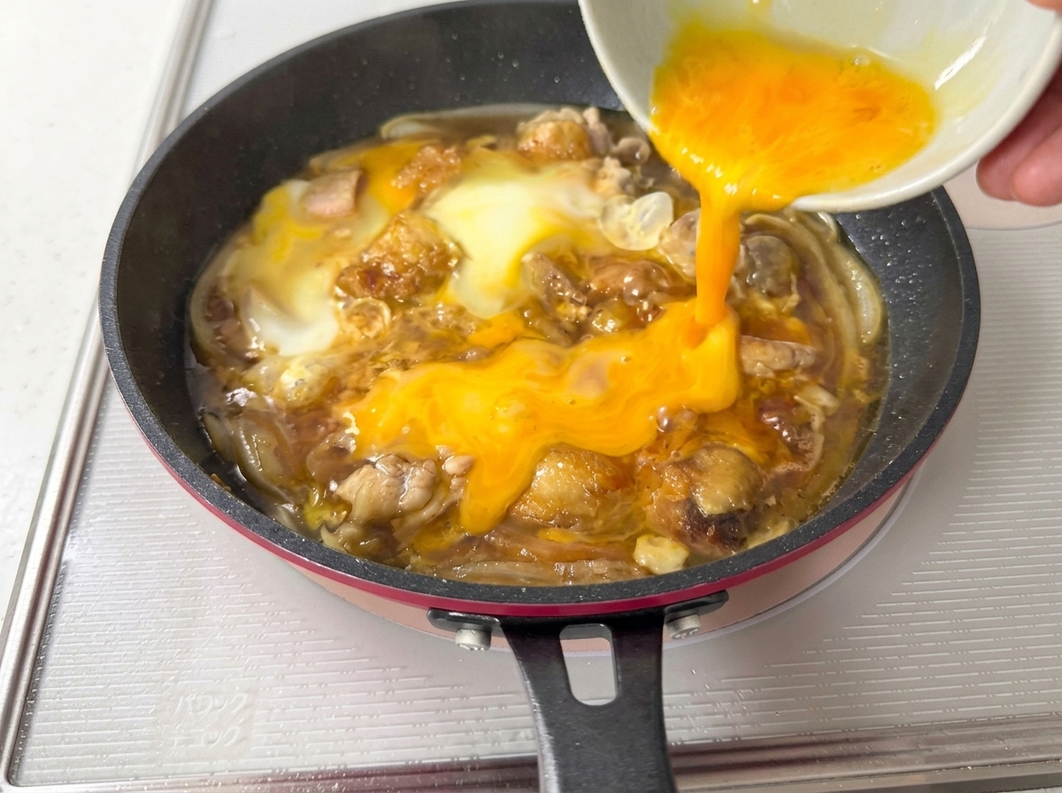 The remaining beaten eggs being poured into the pan, covering the partially cooked ingredients.