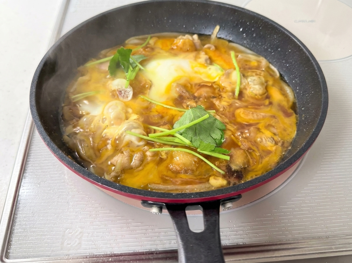 Fresh green mitsuba leaves scattered over a pan of soft-set egg and chicken.