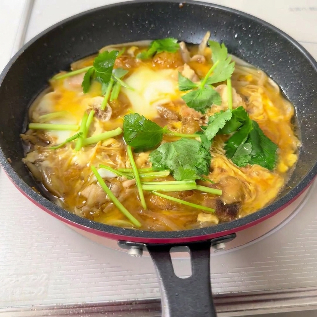 A pan full of cooked Oyakodon mixture being poured over a bowl of white rice.