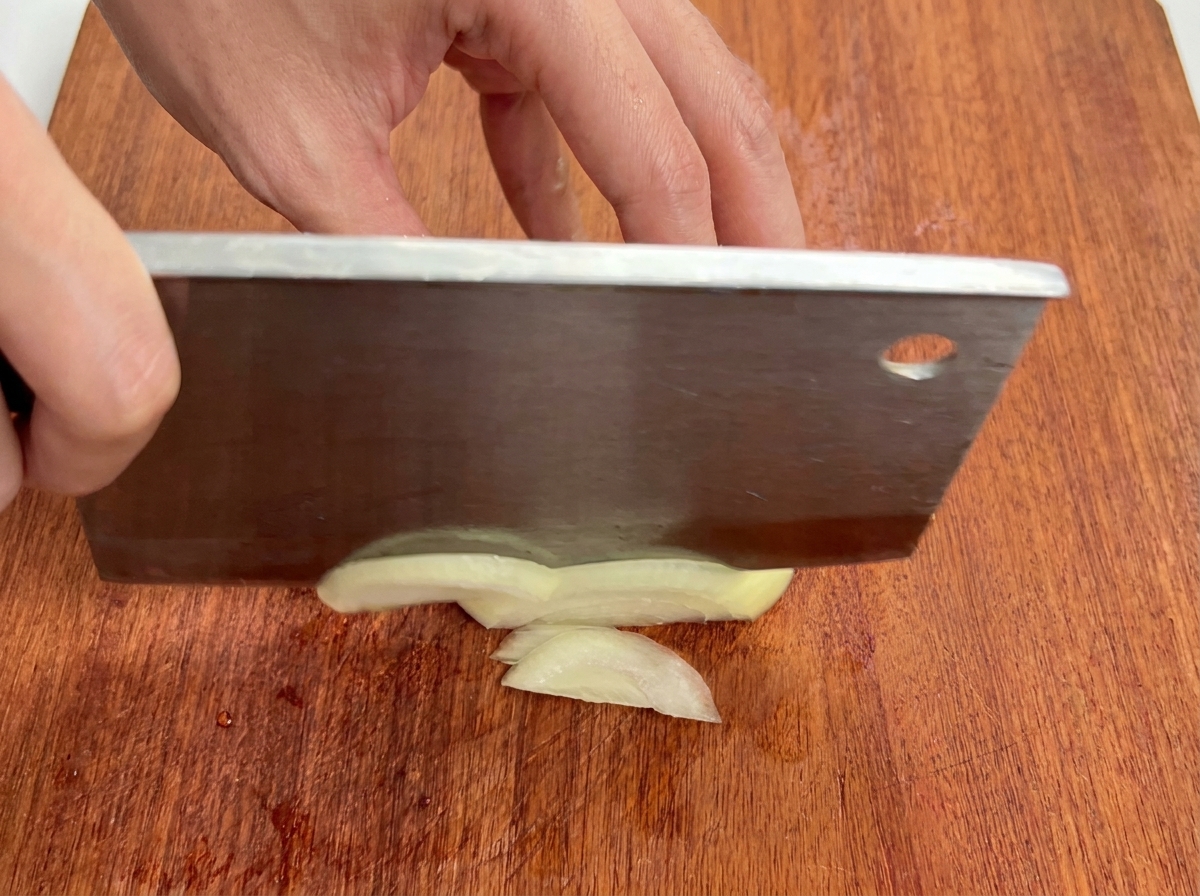 Close-up view of a white onion being cut into thin strips on a wooden cutting board.