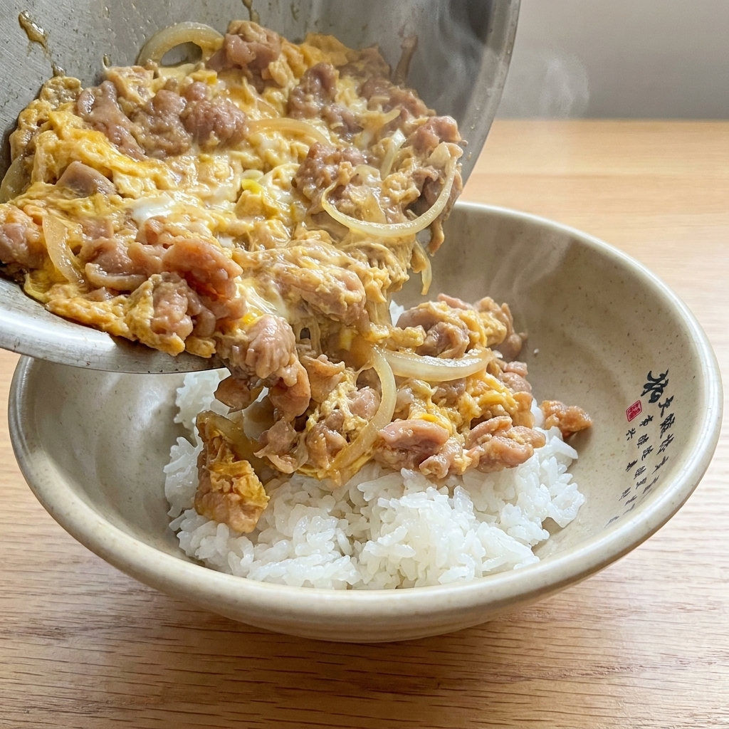 The finished Tanindon dish served in a bowl, featuring a topping of cooked pork, sliced onions, and soft-set eggs over fluffy white rice.