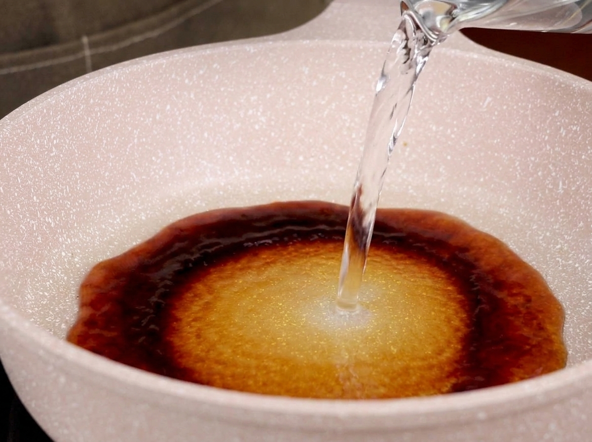 Water being poured into a pan with teriyaki sauce, forming a mixture.