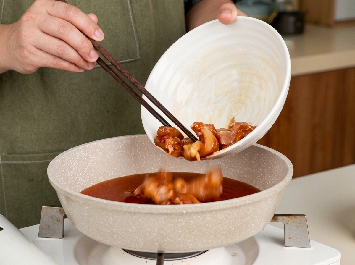 Chicken pieces being added to a pan with teriyaki sauce using chopsticks.