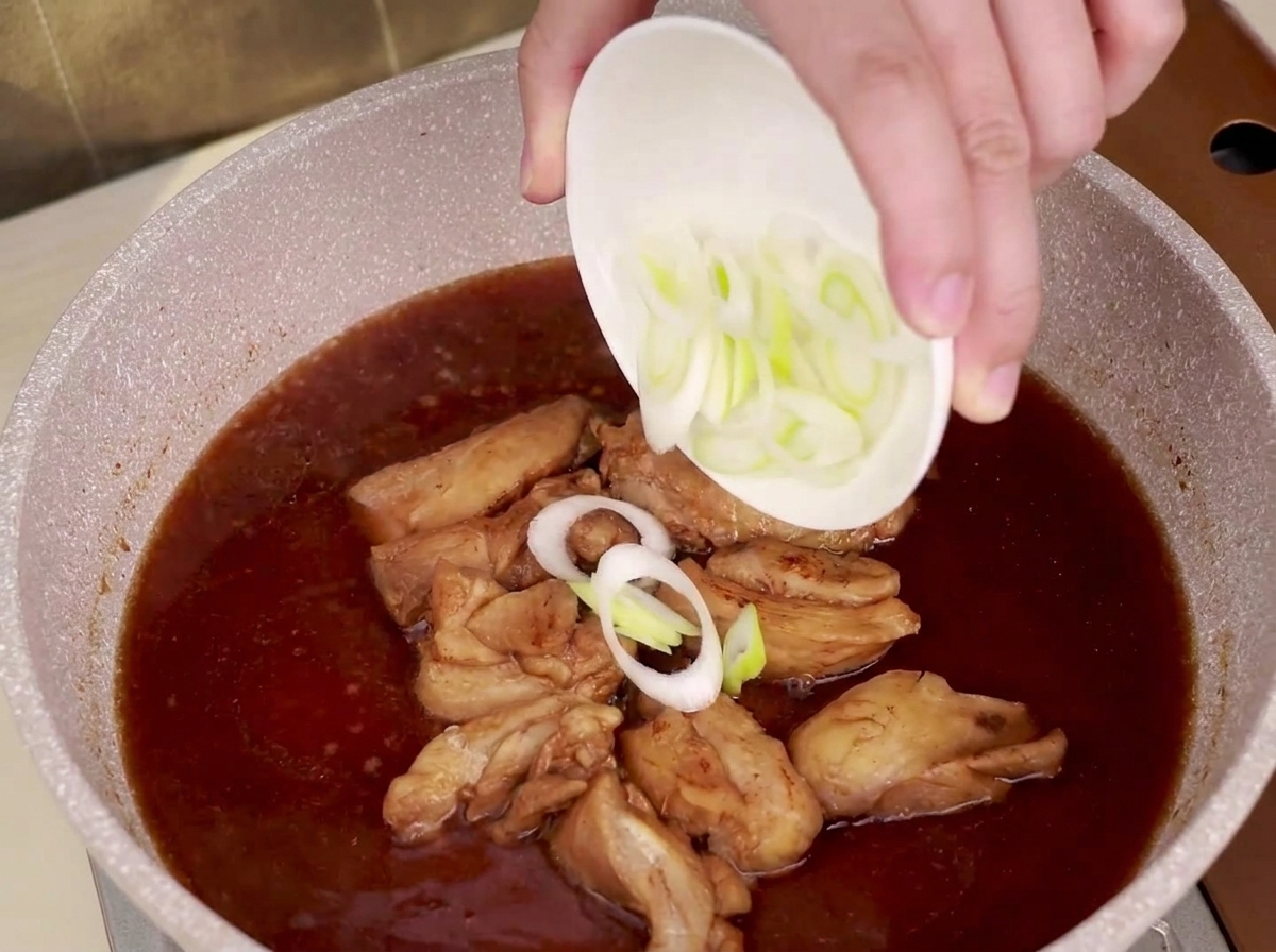 Sliced leeks being sprinkled into a pan of simmering chicken and teriyaki sauce.