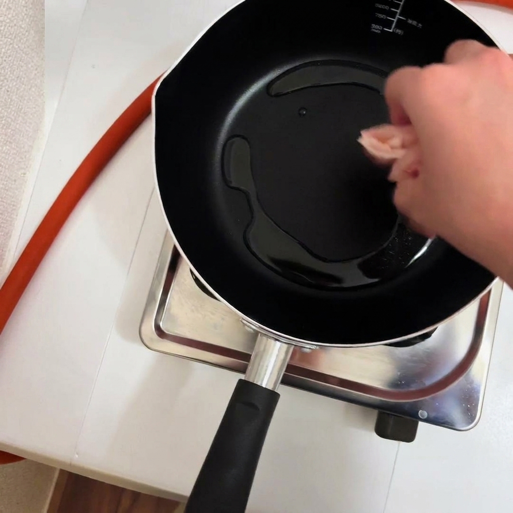 Bite-sized chicken pieces being added to a pan with hot oil.
