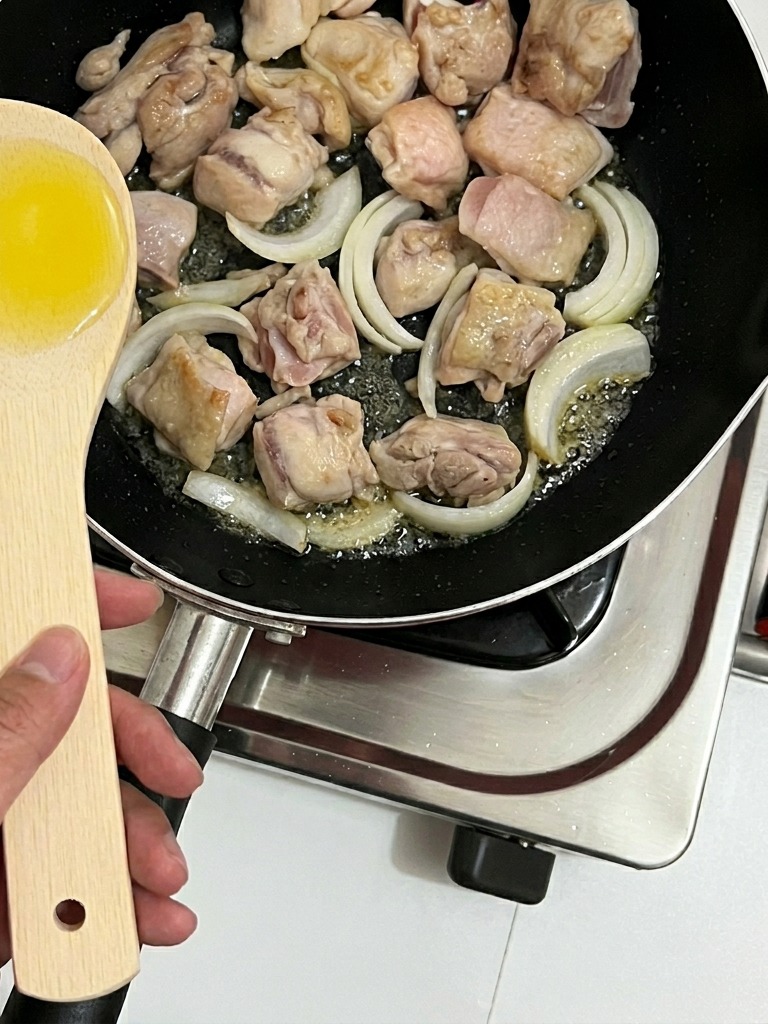 Onion strips being stirred into the pan with chicken pieces.