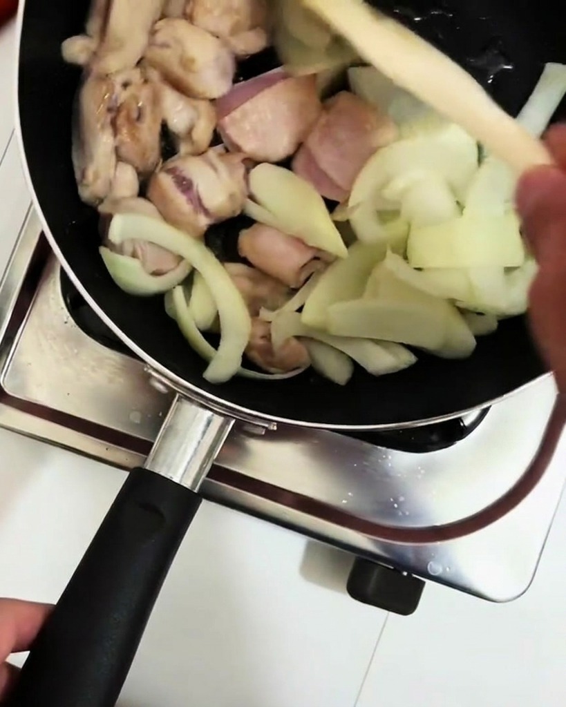 Cooking wine being poured from a ladle into the pan with chicken and onions.