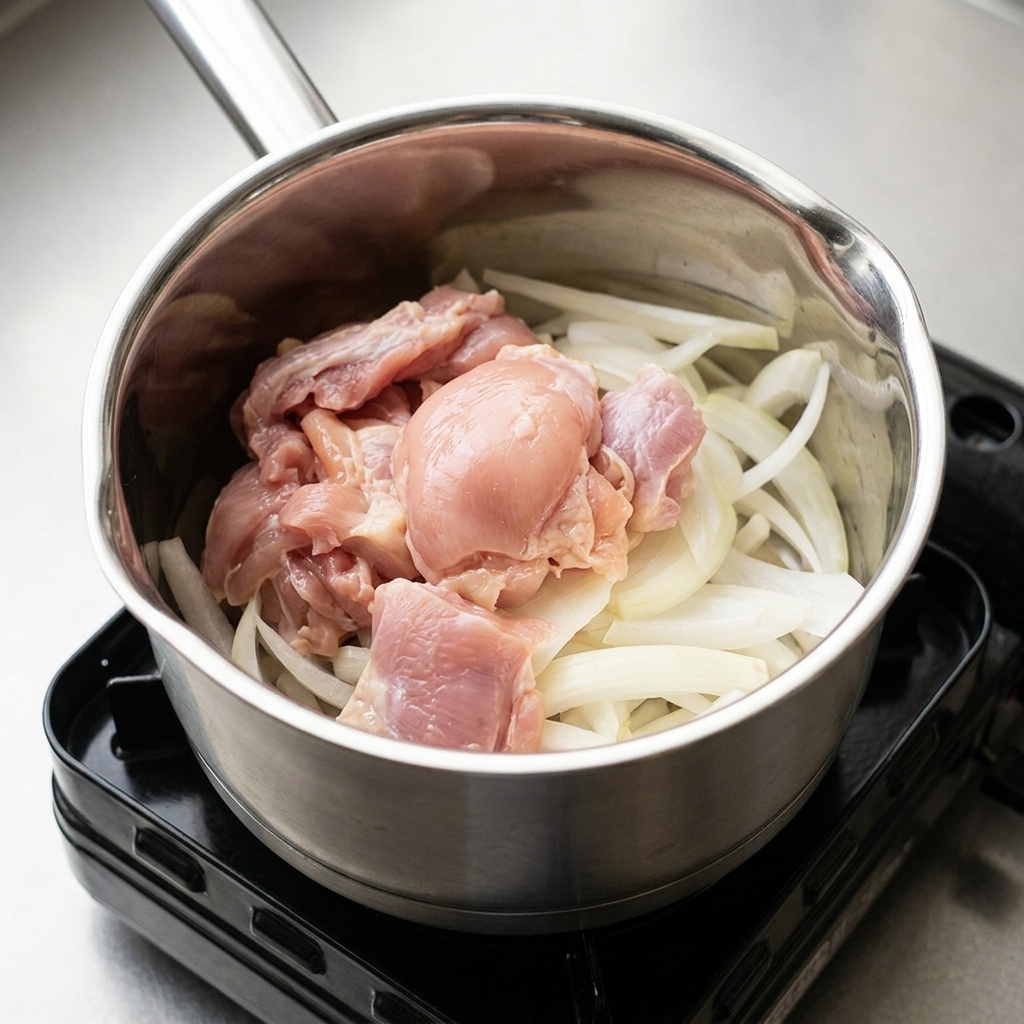 Ingredients including sliced onions and raw chicken pieces in a pot, being seasoned with liquid condiments.