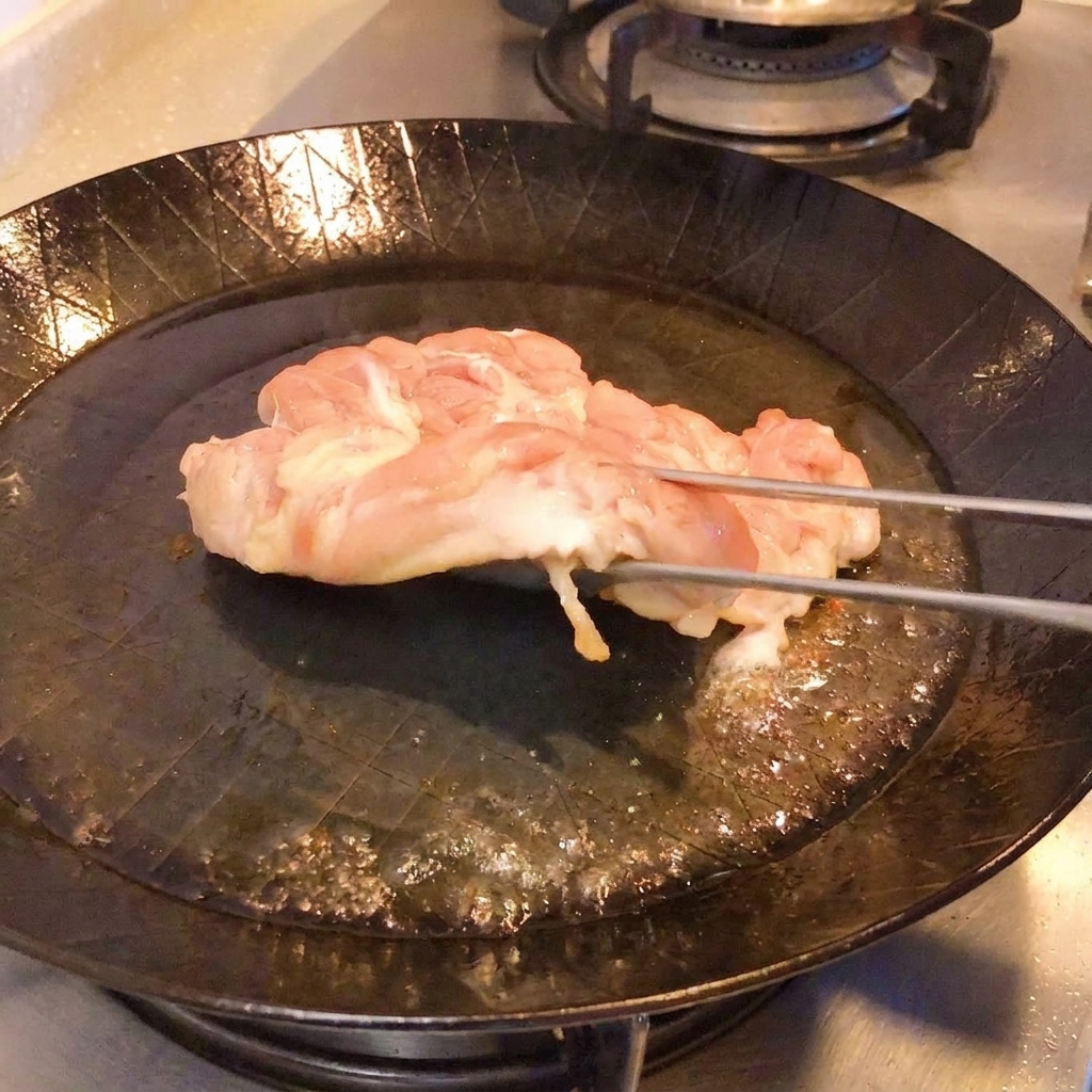 Tongs lifting chicken in a pan to show crispy golden-brown skin.