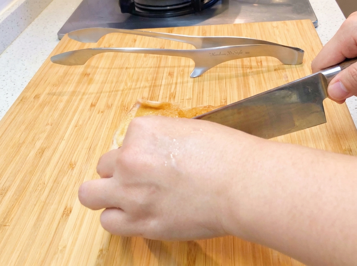 Pan-fried chicken being sliced into bite-sized pieces on a cutting board.