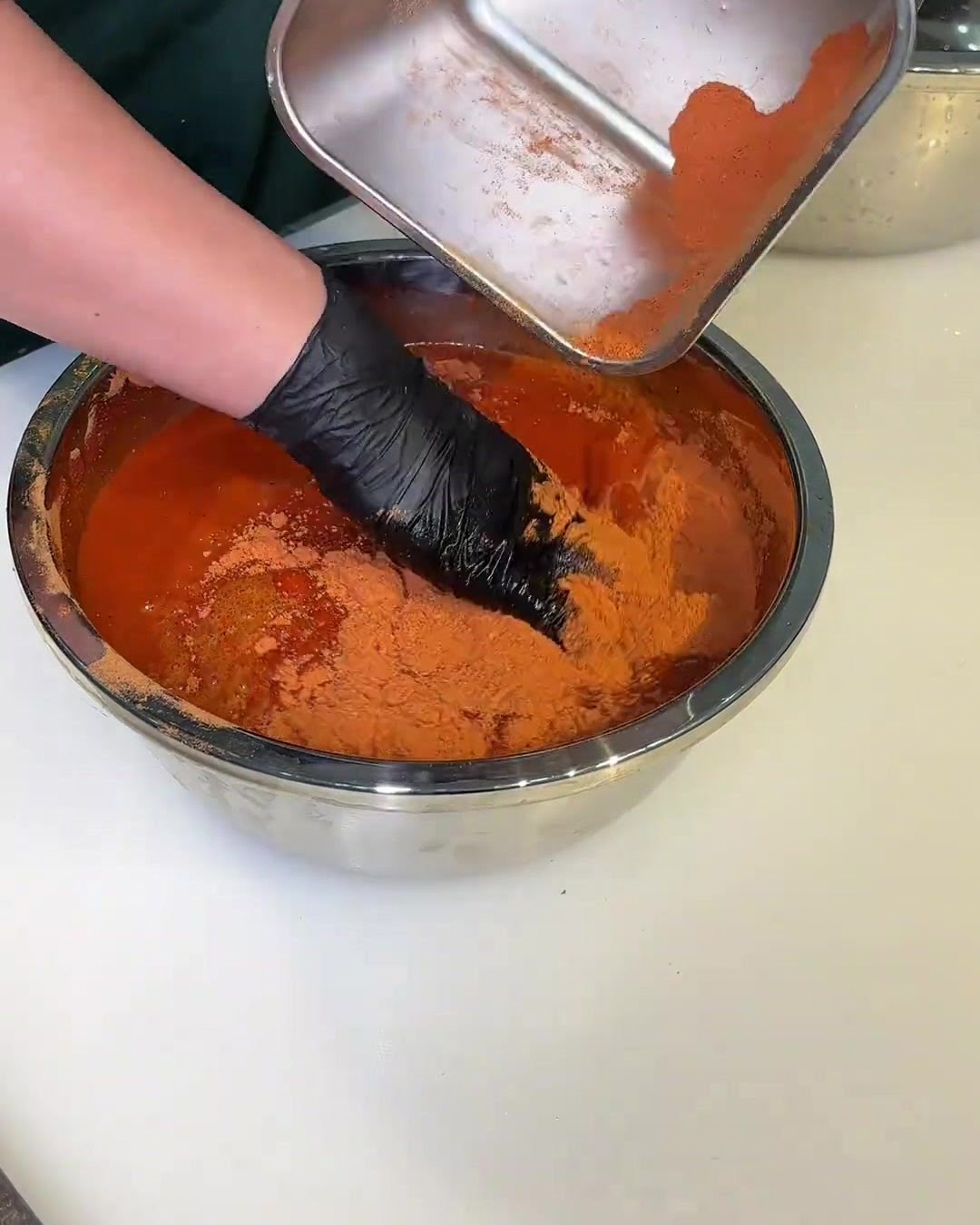 A bowl filled with red marinade sauce, with a gloved hand stirring the pork slices to coat them evenly.