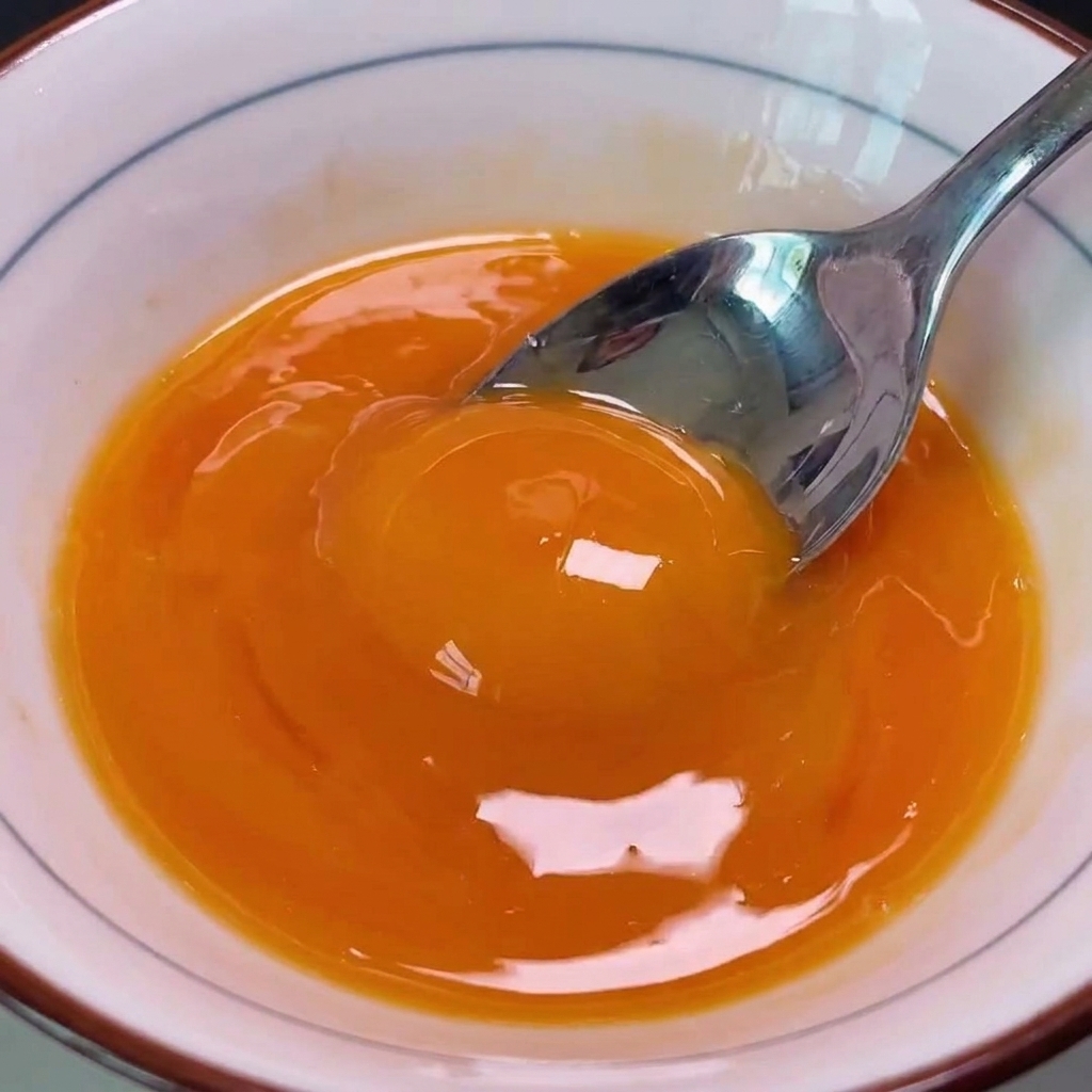 A bowl of vibrant, beaten golden egg yolks being poured over the pork chop and onion mixture in a hot pan.