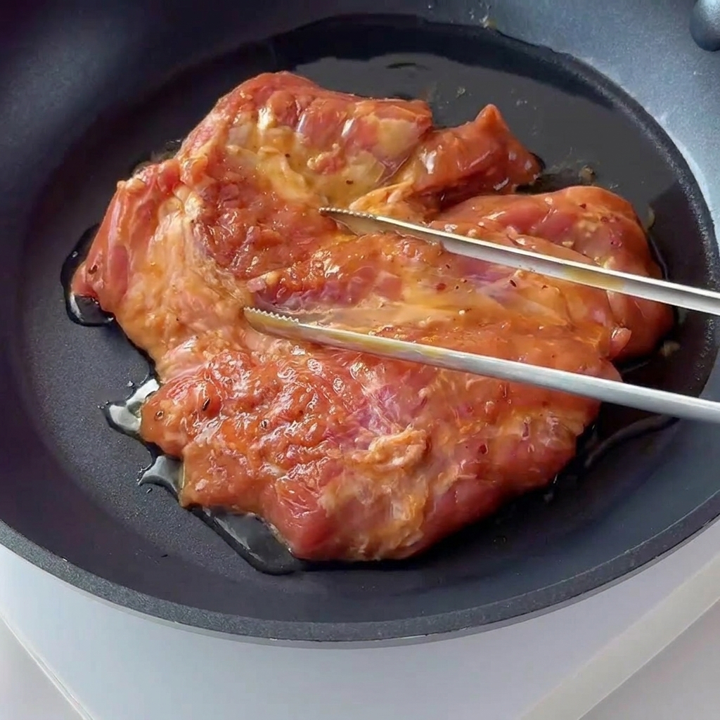 A seasoned pork chop sizzling and browning in a dark non-stick frying pan.