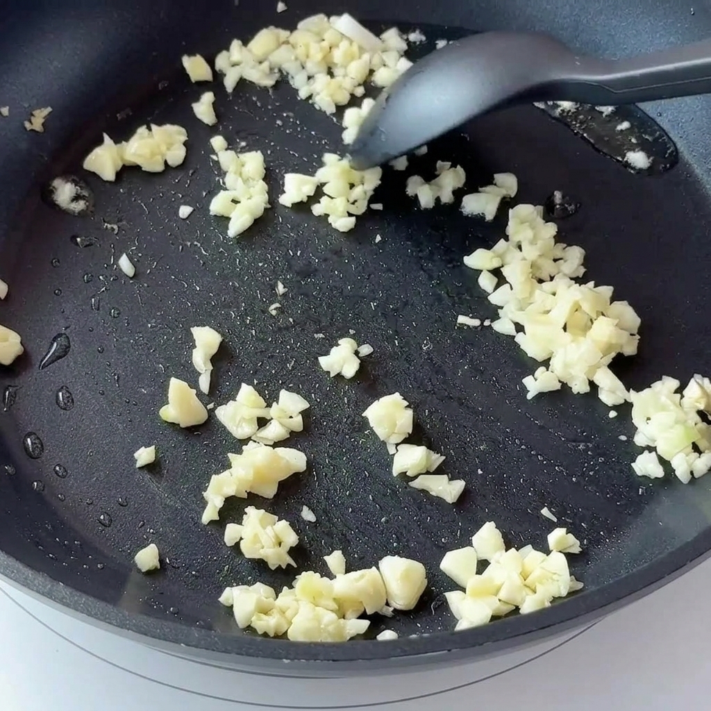 Minced garlic and diced onions frying in a dark non-stick pan.