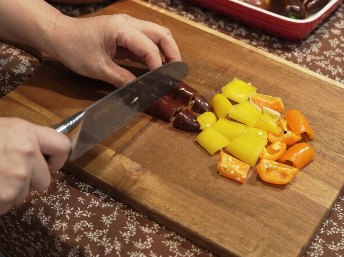 Bell peppers and onions being cut into small pieces on a wooden board.
