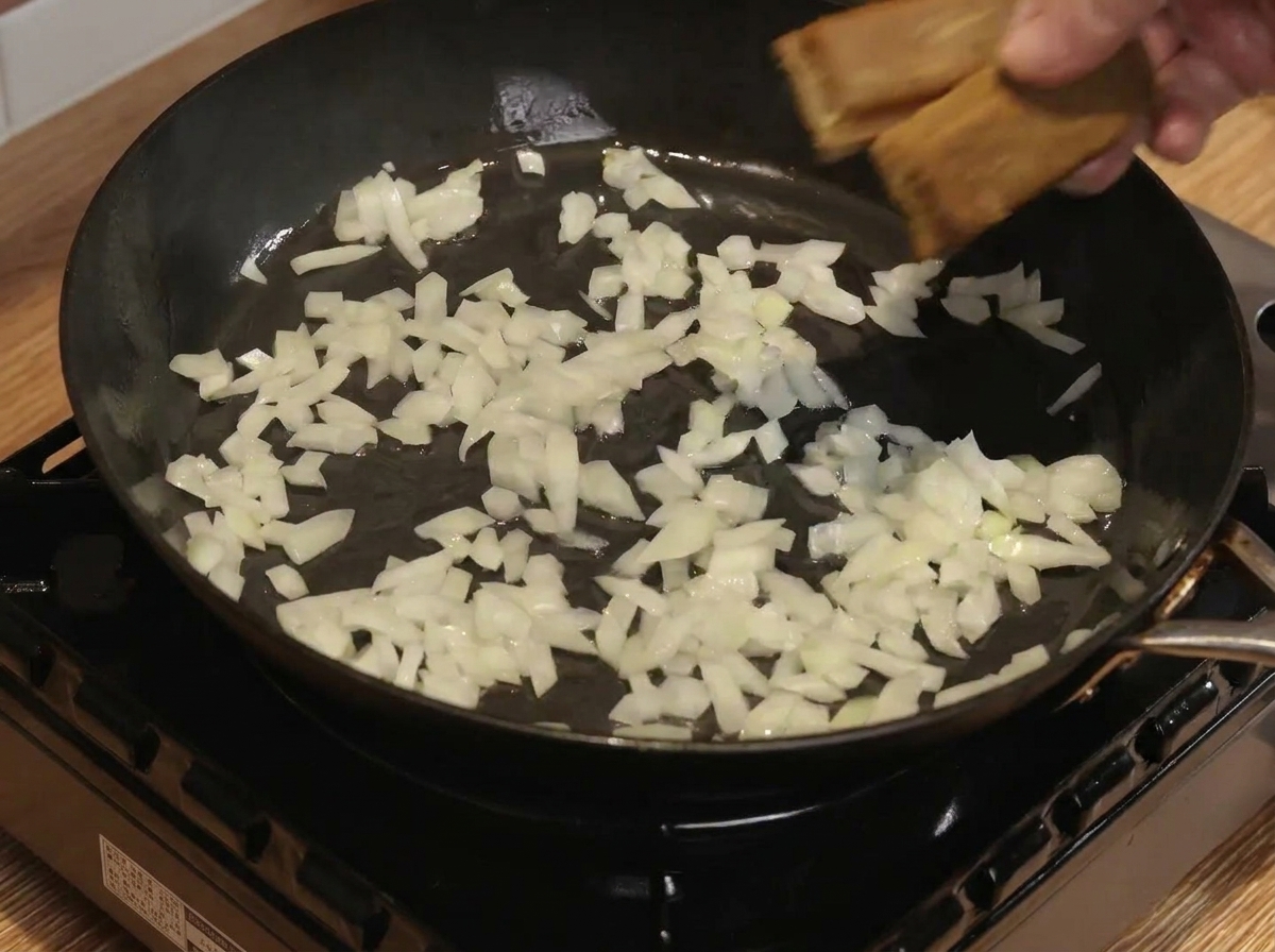 Curry blocks and water being mixed with sautéed onions in a pan.