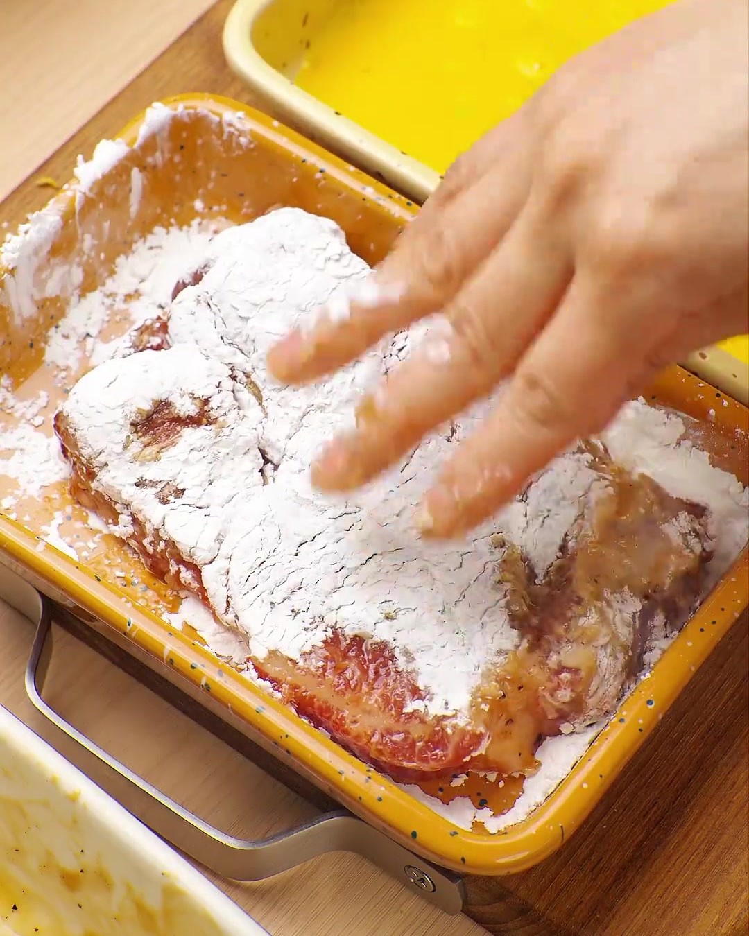 A hand pressing a pork chop coated in egg into a tray of panko breadcrumbs, ensuring full coverage.