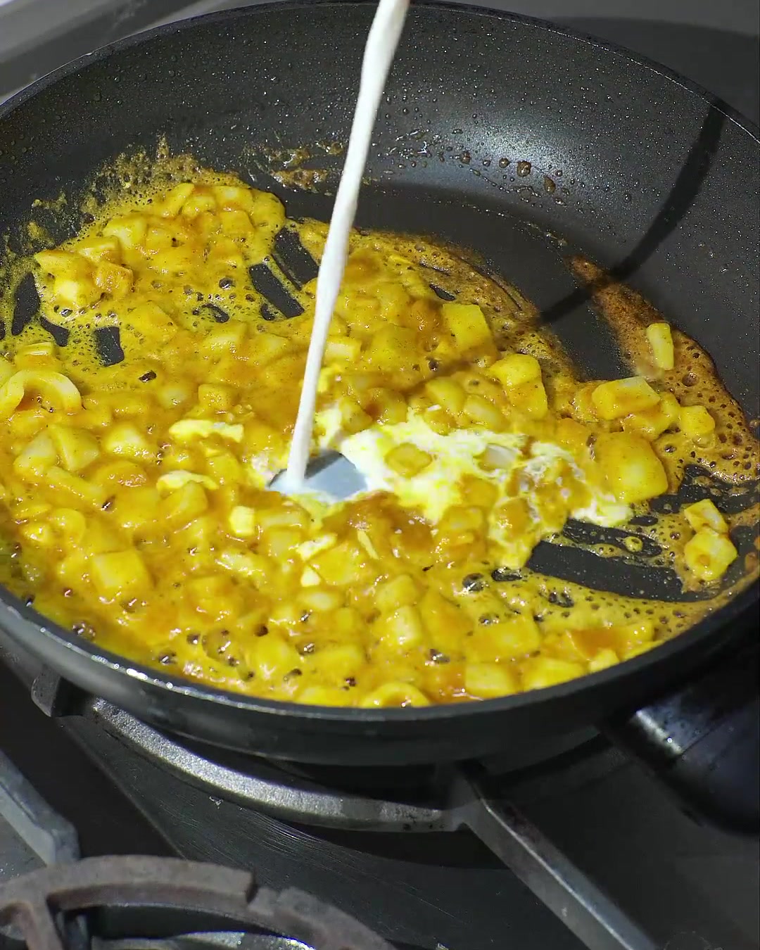 Coconut milk being poured into a skillet with melted curry and sautéed onions, creating a creamy yellow sauce.