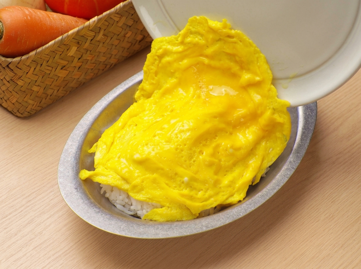 Soft, fluffy scrambled eggs being slid from a pan onto a serving bowl filled with white rice.