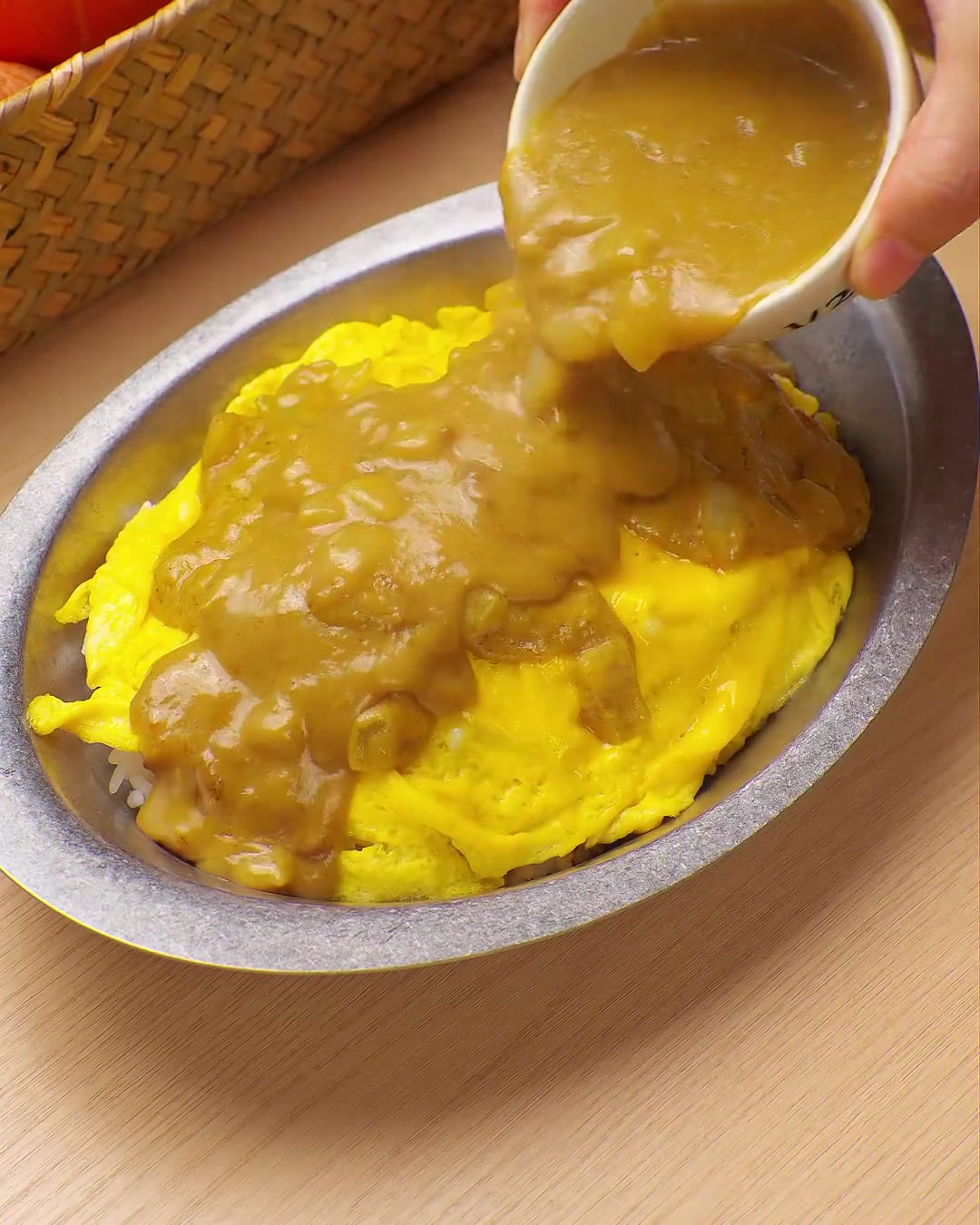 Rich, yellow curry sauce being poured from a small bowl over a bed of scrambled eggs and rice.