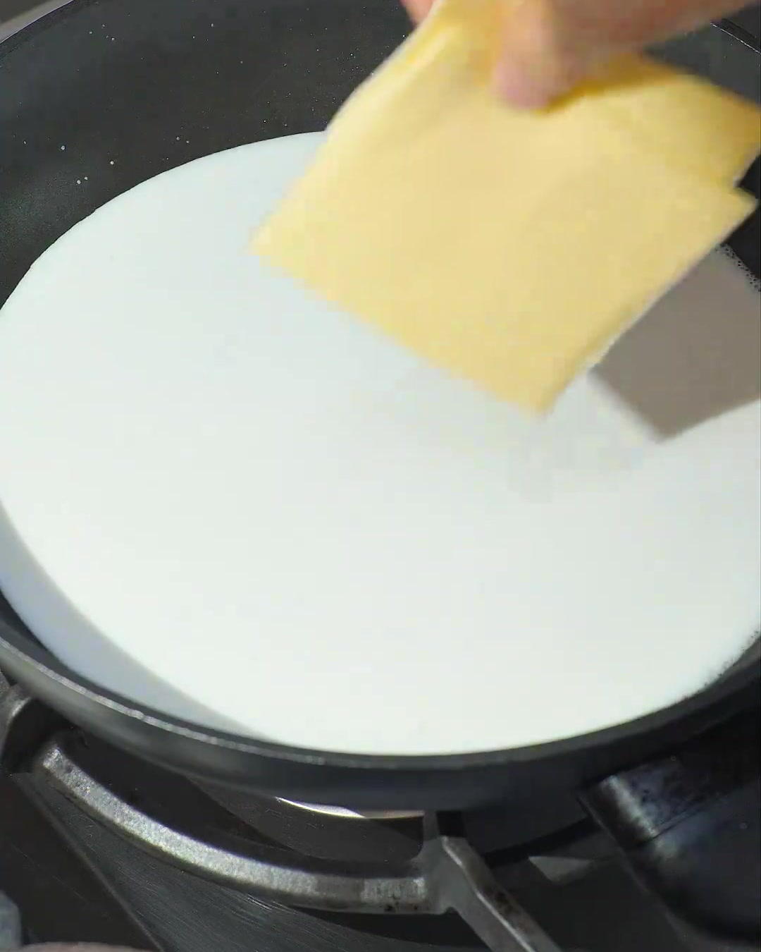 Two slices of yellow cheese melting into simmering white coconut milk in a dark pan.
