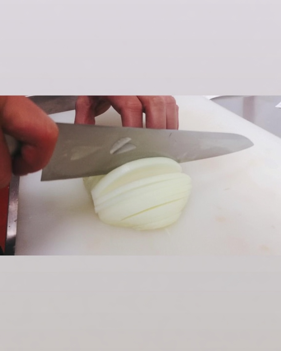 Slicing a raw white onion with a large knife on a white cutting board.