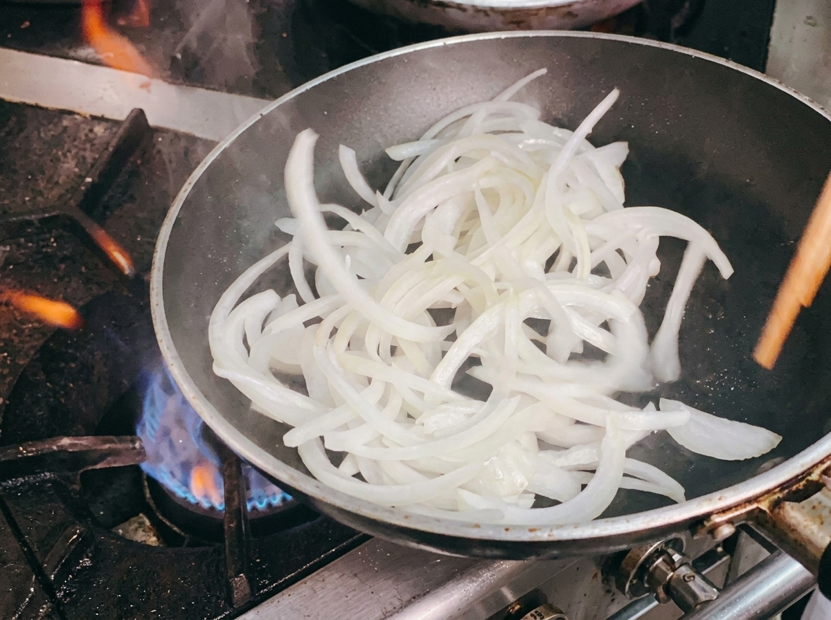 Stir-frying the sliced white onions in the pan using wooden chopsticks.
