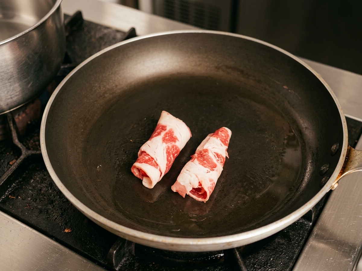Pan-frying rolled slices of raw fatty beef in the hot pan.
